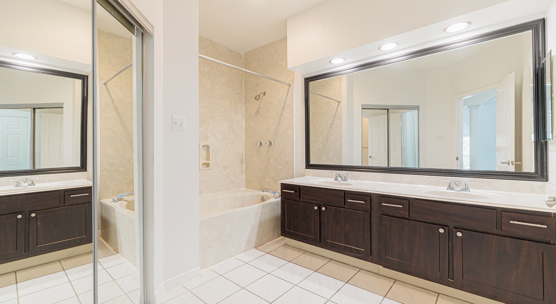 large bathroom with large mirrors wood cabinets sinks and tub